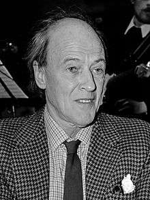 A greyscale picture of Roald Dahl wearing a shirt, tie, and sports jacket