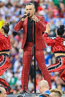 A Caucasian man wearing a red suit with black shirt, performing on stage.