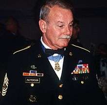 A gray-haired white man wearing a formal military uniform with a star-shaped medal hanging from a ribbon around his neck