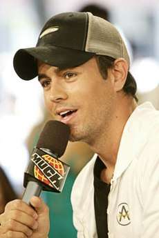 A man with a hat, sweatshirt and a microphone in hand.