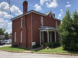 A two-story red brick building with a one-story porch, a hipped roof and three chimneys.