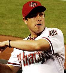 An olive-skinned man wearing a white baseball jersey with maroon and black trim and "D-backs" across the chest and a maroon baseball cap with a stylized "D" on the face