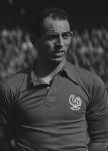 A black and white photography of a light-skinned man wearing a shirt with a rooster on the left chest.