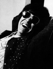 A dark-haired man wearing dark glasses and grinning broadly