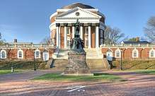 A green statue on a brown pedestal in front of a red brick, Neoclassical dome with a large portico on the front and covered walkway on the sides..
