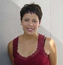 A woman with short brown hair and a red top is smiling toward the camera.