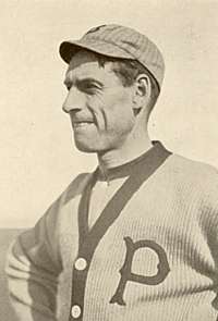 A sepia-toned image of a man wearing a button-down sweater with a "P" on the left breast and a crownless pinstriped baseball cap