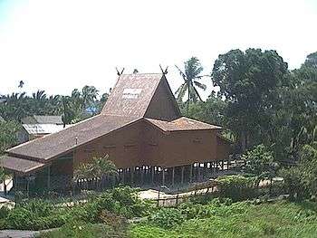 A large wooden house on high piles with a steeply sloping gabled roof