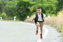 A young boy running in a road. He has black hair and is wearing a backpack.
