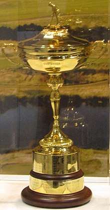 A gold cup set against a background of a lake and fields