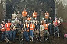 Group photo, showing Second Avenue Subway construction workers posing in front of a tunnel boring machine. The machine has just completed its tunneling to an existing tunnel.