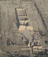 Rectangular stone building from above, with courtyards and pylons at the front and the remains of walls at the back. A rectangular wall and the foundations of other buildings surround the main building.
