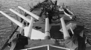 A view of a large battleship's forward guns. There are two turrets of three guns each. The forward turret is turned to port, while the aft turret is facing straight ahead.