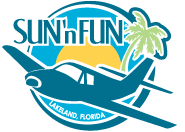 Logo depicts a small plane flying towards the viewer and facing the left. The background consists of two concentric circles (inner is yellow depicting the sun, outer is light blue to represent the sky). On the right is a palm tree and on the left (above the plane) is the name "SUN 'n FUN".