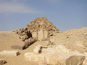 Heavily eroded pyramid with stone blocks and ruins in front