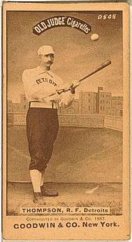 A sepia-toned image of a mustachioed man wearing an old-style baseball uniform holding a baseball bat