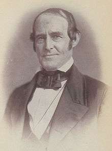 A man in his mid-fifties with thinning, black hair wearing a black jacket and bowtie and a white shirt