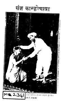 Cover-page of a script titled Saint Kanhopatra (संत कान्होपात्रा) in Marathi, with a photograph showing a woman dressed in a sari kneeling with palms pressed together before a man. The man, dressed in a white dhoti-kurta, is bent forward and seems to be blessing her with his wight hand placed over her head.