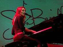 An image of an woman playing a grand piano against a teal background.