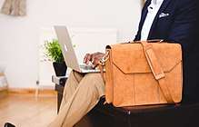 Light-brown leather bag next to man typing on laptop