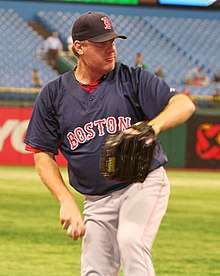 A man wearing a navy blue baseball jersey and cap preparing to throw a baseball with his right hand