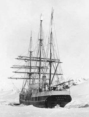  Rear view of a three-masted sailing ship with all sails furled, lying in an ice-covered sea.