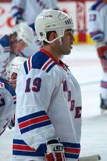 An ice hockey player shown from the waist up on the ice. He is wearing a white jersey with the word "Rangers" in blue across the front.