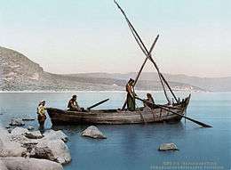photograph of fishermen in a simple boat on a lake, close to a rocky shore