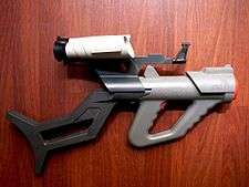 Plastic, gray toy gun with orange highlights and attached black shoulder stock and white scopes.