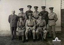 Black and white group photograph of eight men and one woman, all wearing military uniforms.