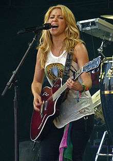 Shakira onstage, singing and playing guitar