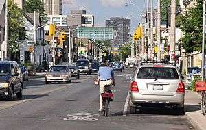 A shared-lane marking in Toronto, Ontario, Canada. Note that the cyclist is not properly positioned on the roadway. Cyclists should ride over the sharrow
