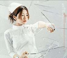 A woman wearing a nurse's outfit punches a pane of glass.