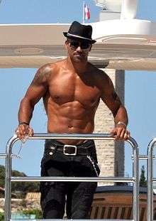 A shirtless man wearing a hat and jeans.