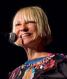 A Caucasian woman with short blond hair, smiling on stage.