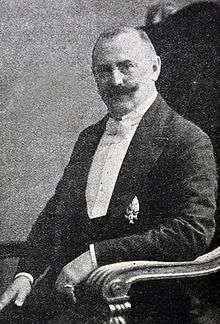 Photo of Siegfried Translateur, sitting, wearing a white tie, a medal and a handlebar moustache.