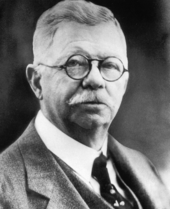 An early 20th century photo of a middle-aged man with glasses, a mustache, and a suit.