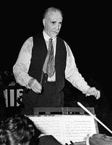 elderly, balding man with short white moustache and beard, conducting an orchestra