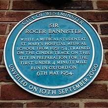 Blue circular plaque which reads: City of Westminster – unveiled on 10th September 2000 – Sir Roger Bannister – while a medical student at St. Mary's hospital medical school from 1951–54, trained on the cinder track on this site in preparation for the first under 4 minute mile run in Oxford on 6th May 1954.