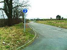 Narrow single carriageway, with wide grass verges, in a flat rural landscape