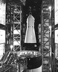 Black-and-white picture from inside a tall building with a space capsule being lifted from the top of a rocket