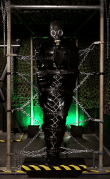 A model is held inside a rubber sleepsack and chained up to a bondage frame as part of restrictive bondage play.