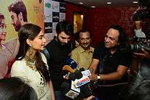 Khan and Sonam Kapoor in front of a bank of microphones and cameras