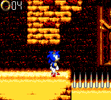 Sonic, a cartoonish blue hedgehog, stands in a desert environment. Spikes can be seen in front of him, and a counter displaying rings is in the upper left-hand corner.