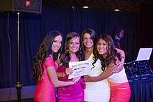 Four young women pose holding both each other and an award for "Alpha Gamma Delta: Best Tree"