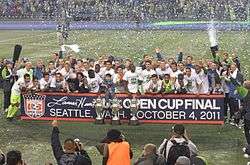 Several players are standing together with three trophies on the ground in front of them.