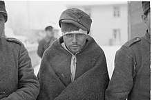 Soviet prisoners of war keep warm with their new clothes. The prisoner in the middle of the photo is staring at the ground with hollow eyes.
