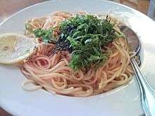 A white bowl of spaghetti in red sauce, garnished with minced nori and julienned shiso leaves