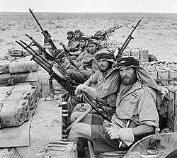 A close-up of six men in three Jeeps. A heavily armed patrol of 'L' Detachment SAS. The crews of the Jeeps are all wearing 'Arab-style' headdress, as copied from the Long Range Desert Group. Jerri cans can be seen mounted around the vehicles