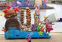 A costumed mascot of Pearl and an animatronic Mr. Krabs standing on a parade float